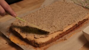 Osoba razmazuje orahovu smesu preko pečenog biskvita