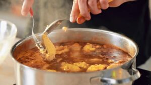 Osoba ubacuje kašikom formiranu knedlu u šerpu sa paprikašom