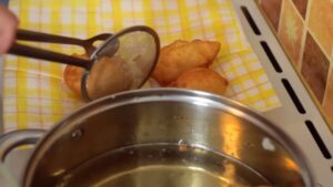 Osoba hvataljkom vadi pržene uštipke iz šerpe